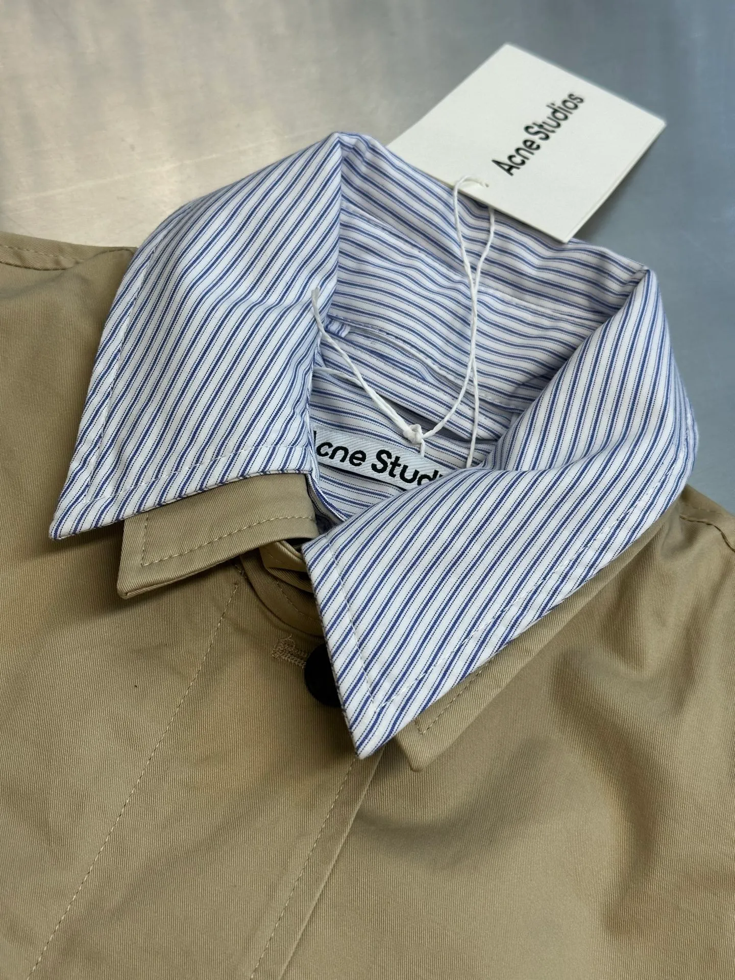 Ac Hot Sale genuine two-piece jacket. The main body is made of high-density twill cotton poplin. It has been processed by pre-shrunk washing process. The cloth surface is smooth and clean, with a matte and soft workwear texture. The stiffness is just right. The short version can be held up three-dimensionally and is not easy to collapse and wrinkle. It is suitable for daily commuting and outdoor use. The inner shirt is made of yarn-dyed blue and white striped cotton. The yarn-dyed stripes have clear texture and will not turn white or smudged after washing. The fabric surface is breathable and dry, and the collar and cuffs are folded and exposed to form contrasting color layers. The difficulty of the whole piece lies in the combined sewing of two fake pieces. The shirt collar and jacket collar are double-stitched and seamed. The collar corners are shaped and hemmed, and the folding shape is neat and will not collapse and curl. The placket adopts a double-layer structure of zipper + hidden buckle windproof fabric. The inner and outer layers of fabric are aligned and sewn together, and the wiring is even and fine. There are adjustable tabs on both sides of the hem, which can be freely tightened to suit different styles. The back printing adopts embossed relief technology, which blends into the fabric and is low-key and unobtrusive. The zipper is made of nylon zipper with metal teeth. The teeth are polished smoothly and will not get stuck after repeated pulling. The zipper headband has brand engraved details. The buttons are divided into two systems: the outer part is made of horn dark brown resin buttons with natural texture and high-end matte texture; the inner shirt is equipped with Cream White pearlescent four-eye buttons, echoing the blue and white striped fabric. size：xs s m l